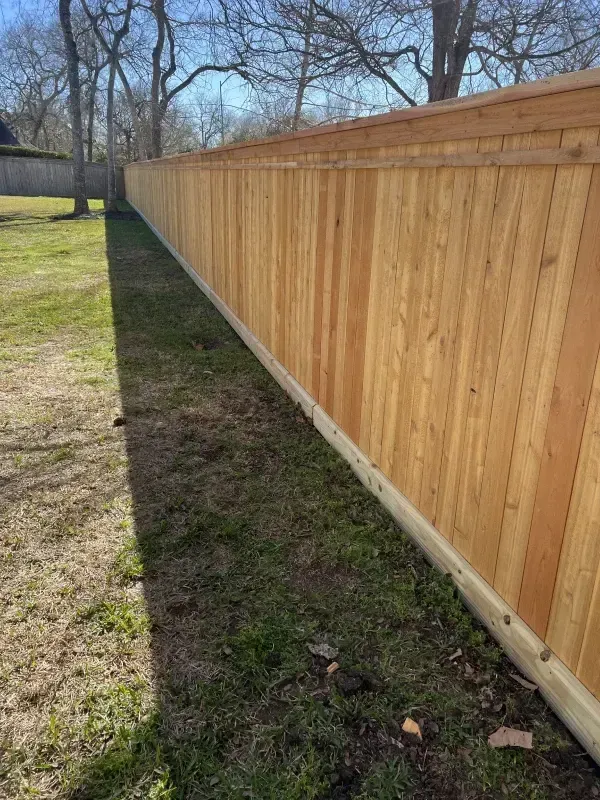 Wooden fence in a grassy yard, with a treeline and blue sky in the background.