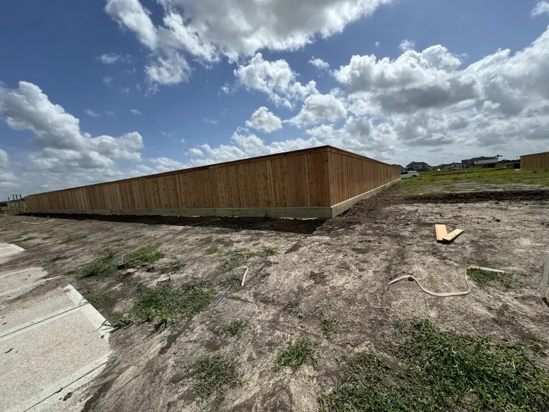 Wooden fence along a dirt lot under a blue sky with scattered clouds.