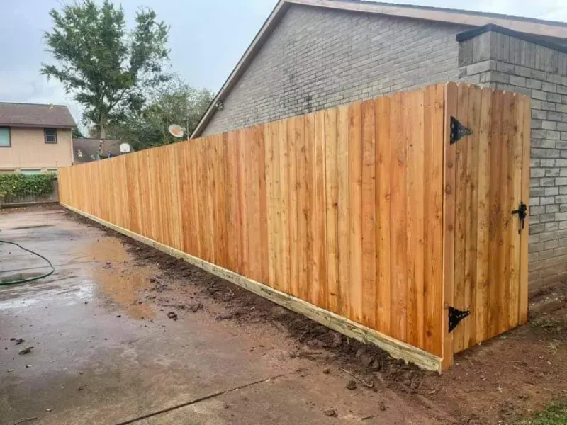 Wooden fence with a gate, next to a brick building, and a driveway.
