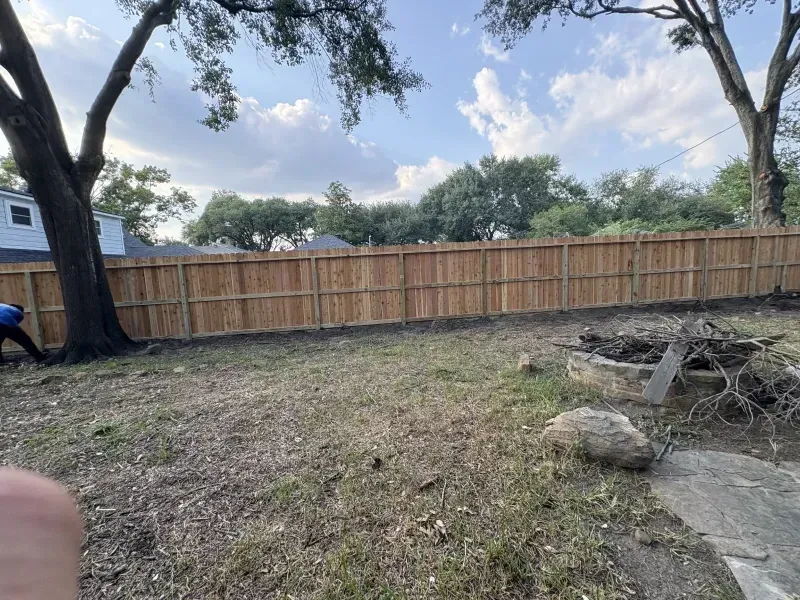 Backyard with a wooden fence. Person working near a tree. Sky with clouds.