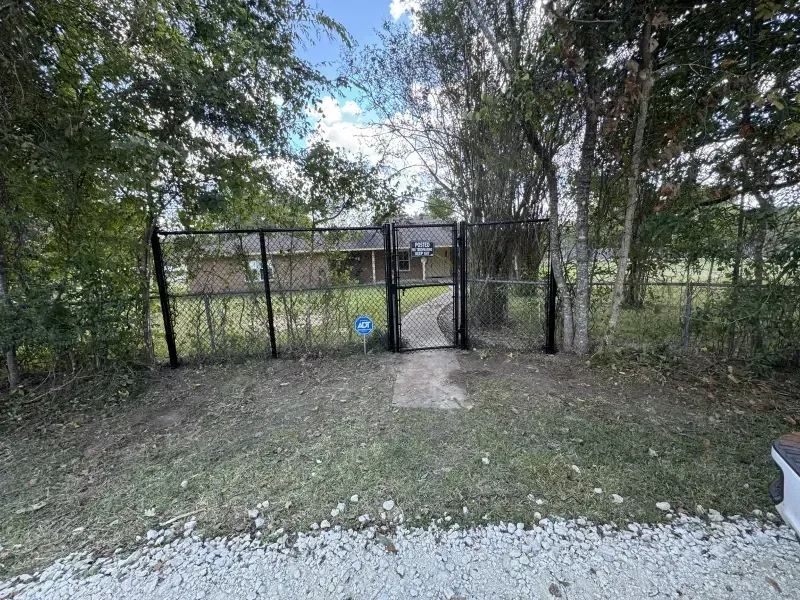 Black metal fence with gate in front of a house, surrounded by trees and grass, on a sunny day.