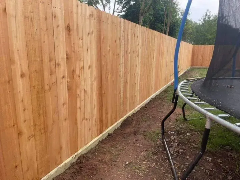Wooden fence alongside a trampoline on grass.