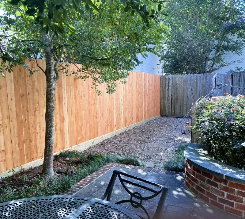 Backyard with new wooden fence, tree, gravel path, brick wall, and green bushes.