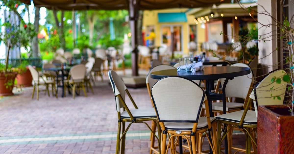 A restaurant's outdoor dining area has several tables, protected under canopies and surrounded by trees.
