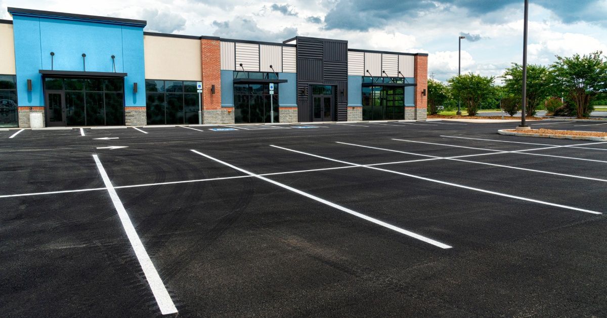 An empty parking lot outside a commercial plaza with newly applied pavement.