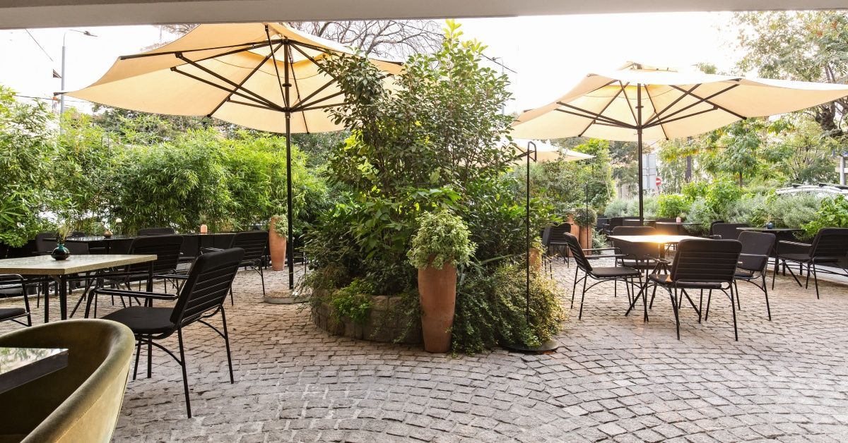 Several tables are set up on a garden patio at a restaurant. The space features cobblestone pavement