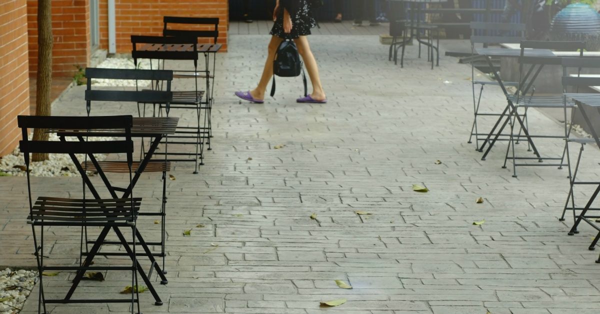 Rows of small tables are set up outside an establishment as a person walks toward it. Tree leaves sway in the wind.