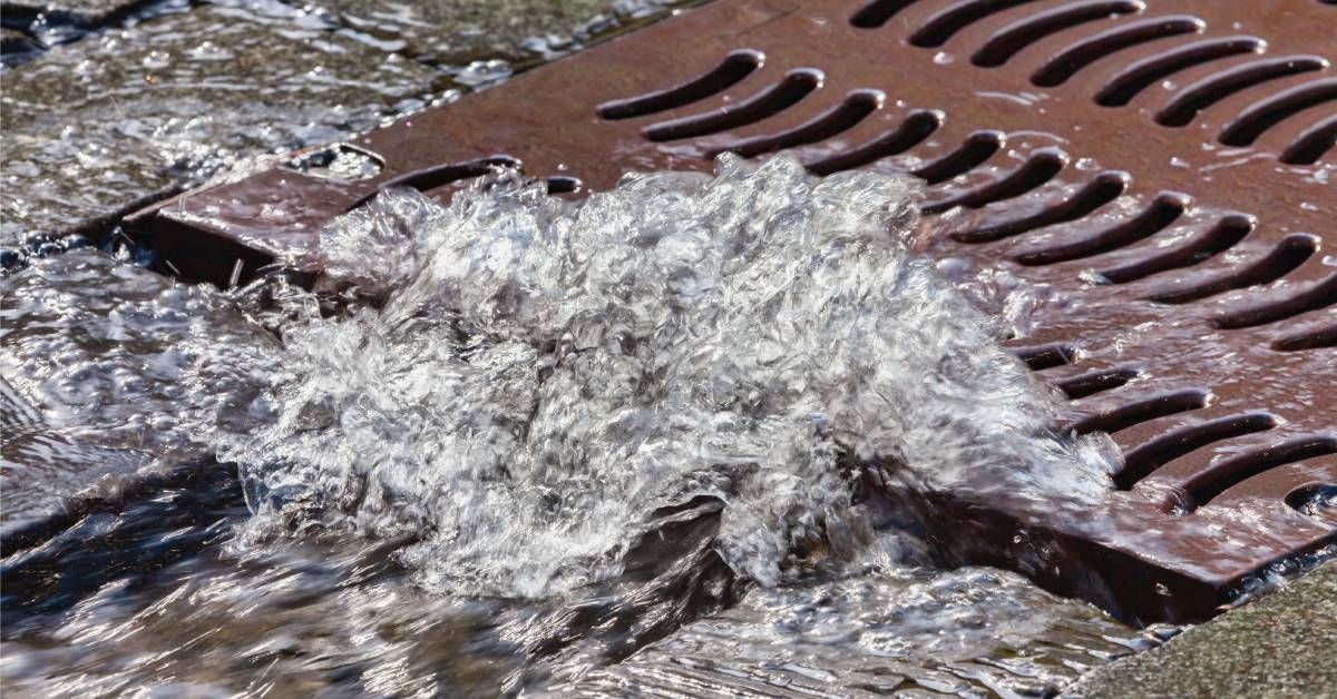 Rainwater running down a sidewalk and into a curb, rapidly rushing and rolling into a city sewer grate.