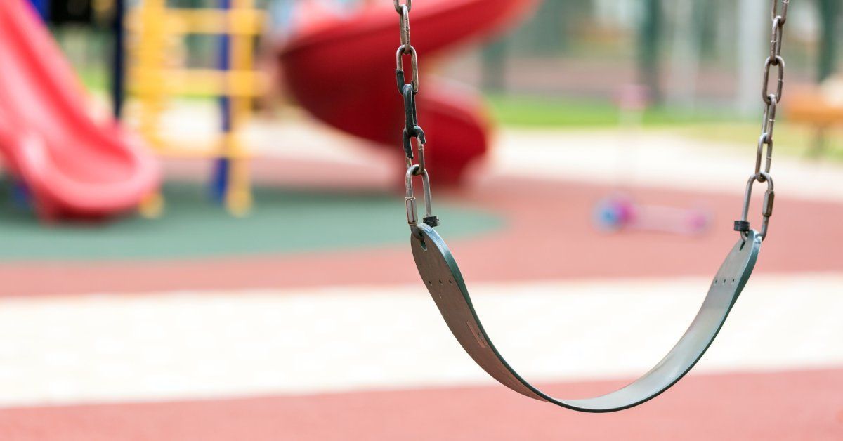 Close up on a black swing in the foreground of a playground that is behind it.