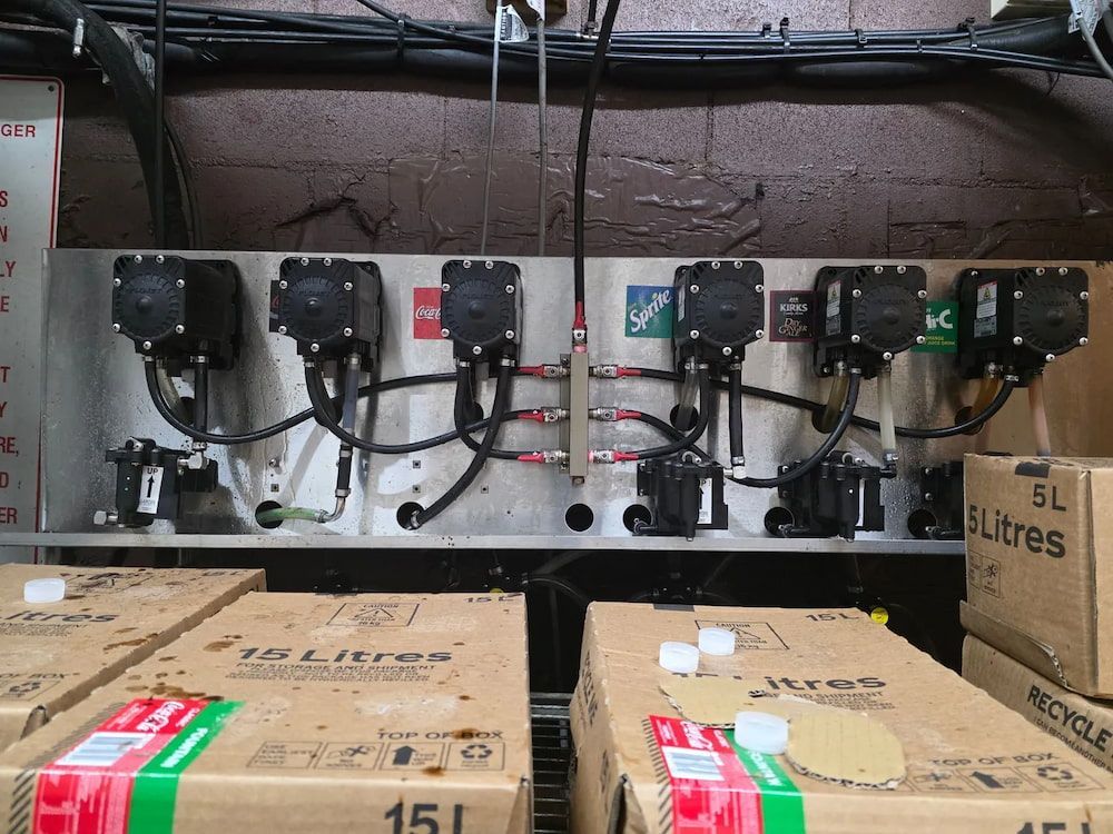 Metal Panel With Pumps and Tubing Above Boxes of Liquid — BNS Refrigeration Services in Healy, QLD