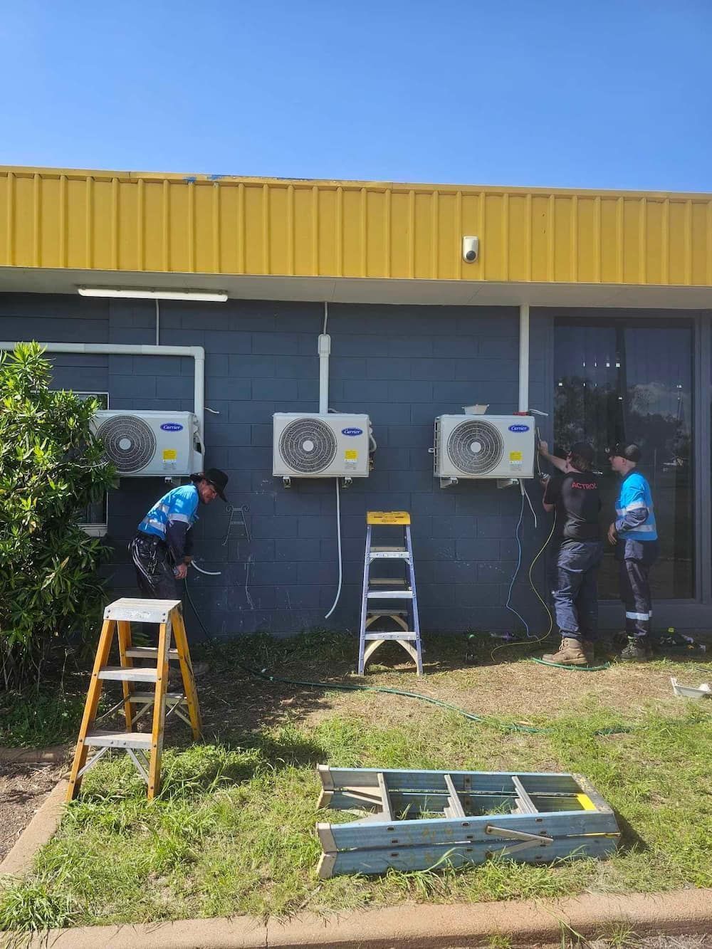 Three People Installing Air Conditioning Units on a Building — BNS Refrigeration Services in Healy, QLD