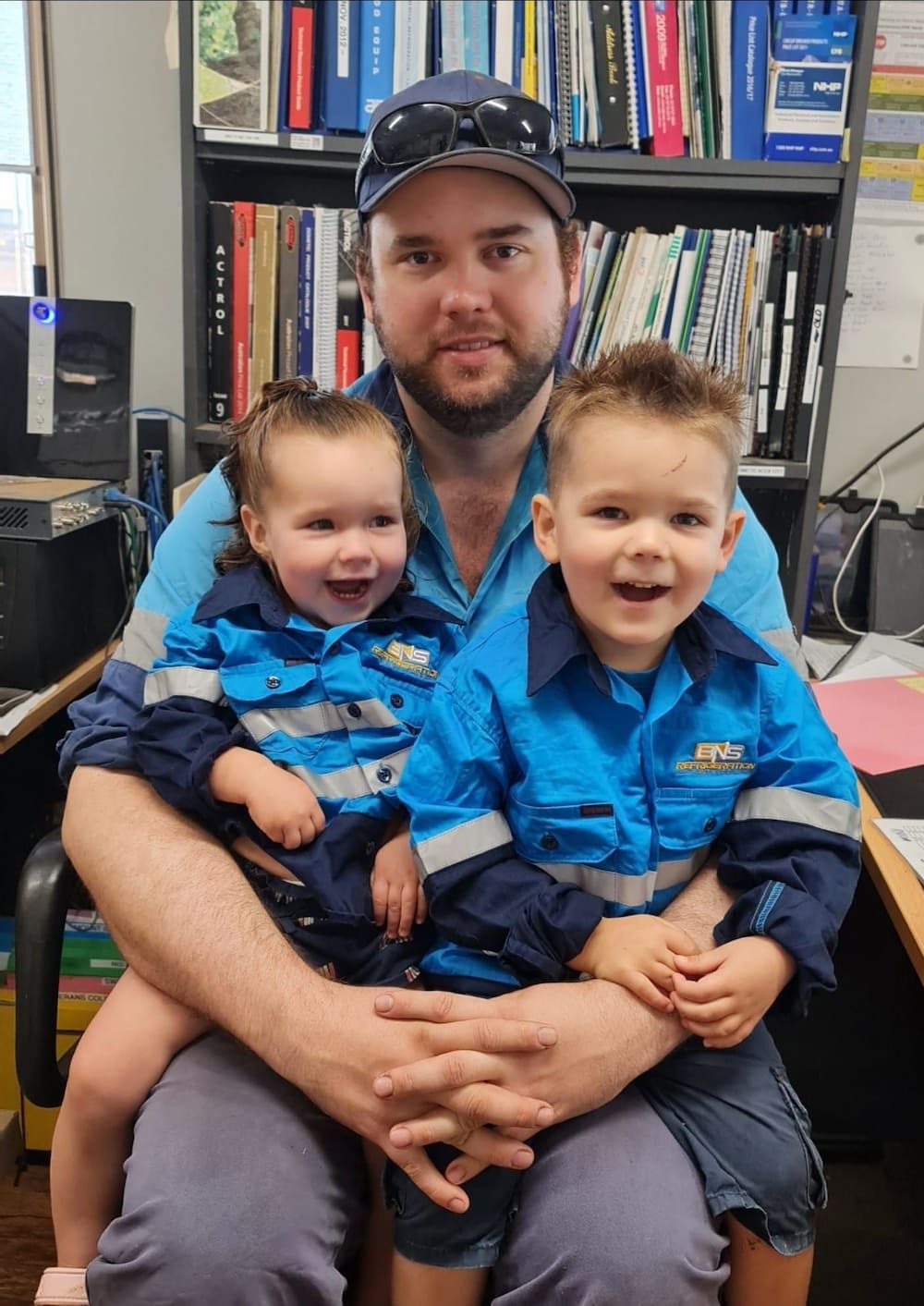 Group of Workers in Blue Shirts Seated Around a Table — BNS Refrigeration Services in Healy, QLD