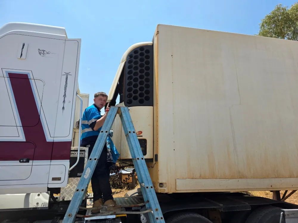 Man on ladder working on the refrigeration unit of a semi-truck trailer outdoors— BNS Refrigeration Services in Healy, QLD