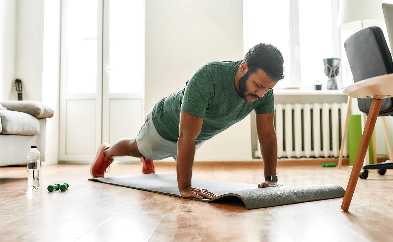 A man is doing push ups on a yoga mat in a living room.