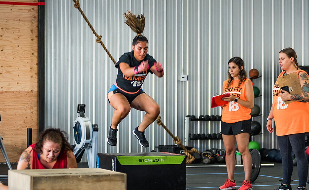 A woman is jumping over a box in a gym.