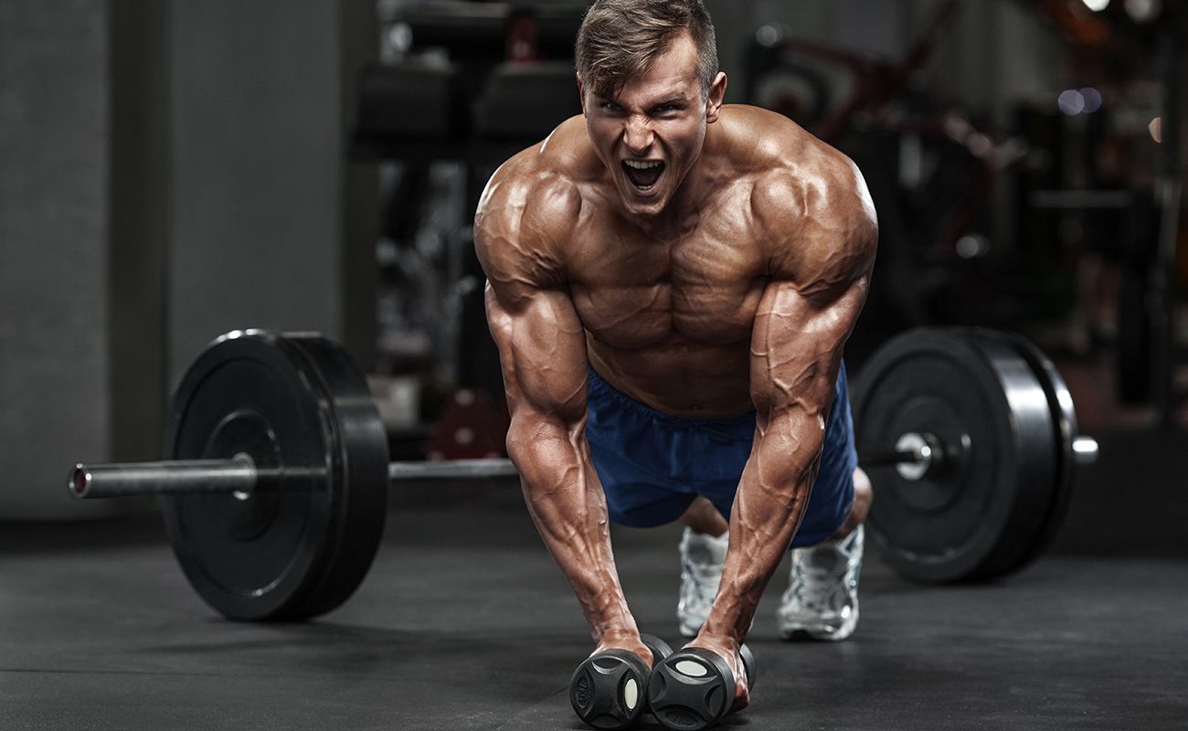 A muscular man is doing push ups with dumbbells in a gym.