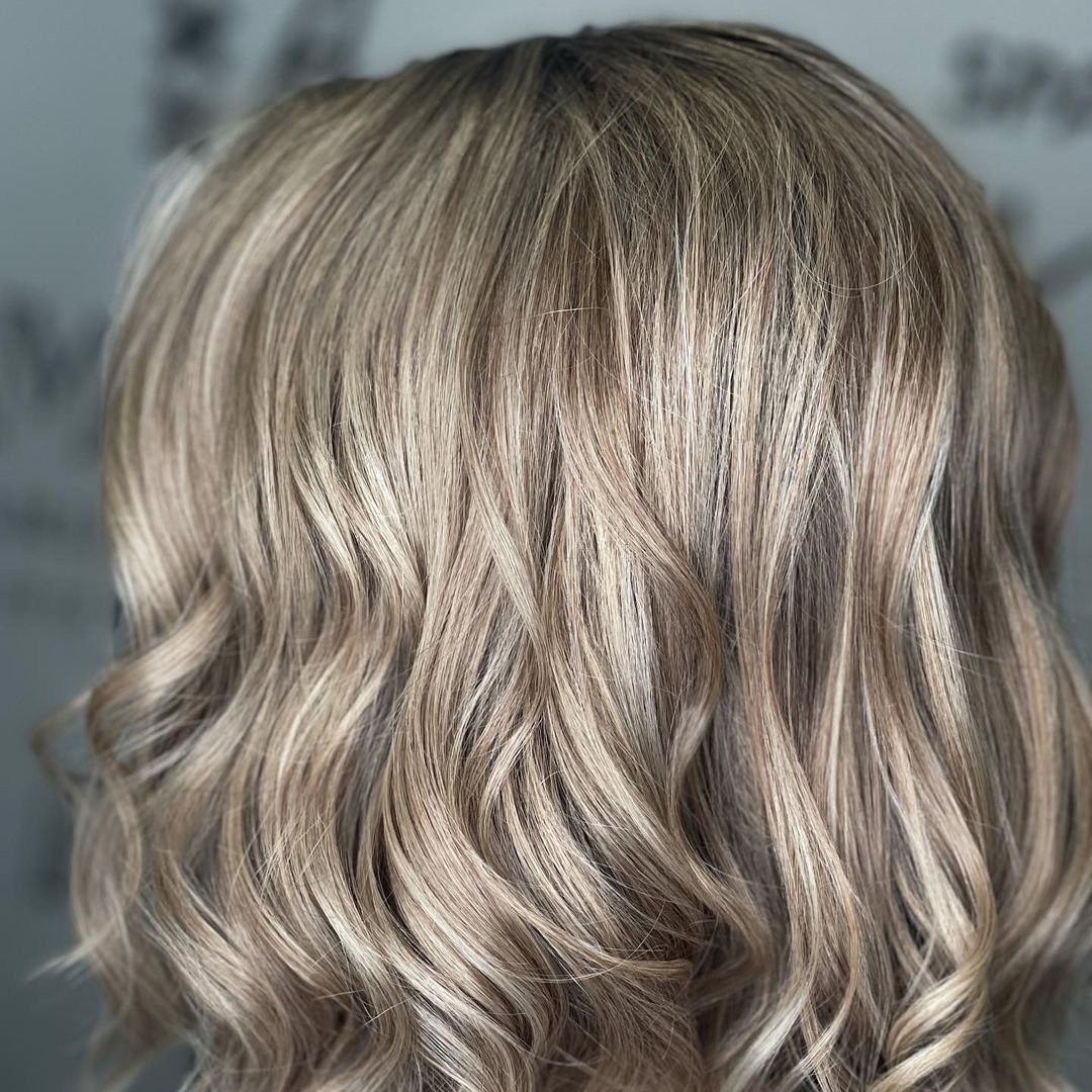A Woman With Long Curly Hair is Holding Her Hair in Her Hand — Sophisticut Hair Salon in Mysterton, QLD