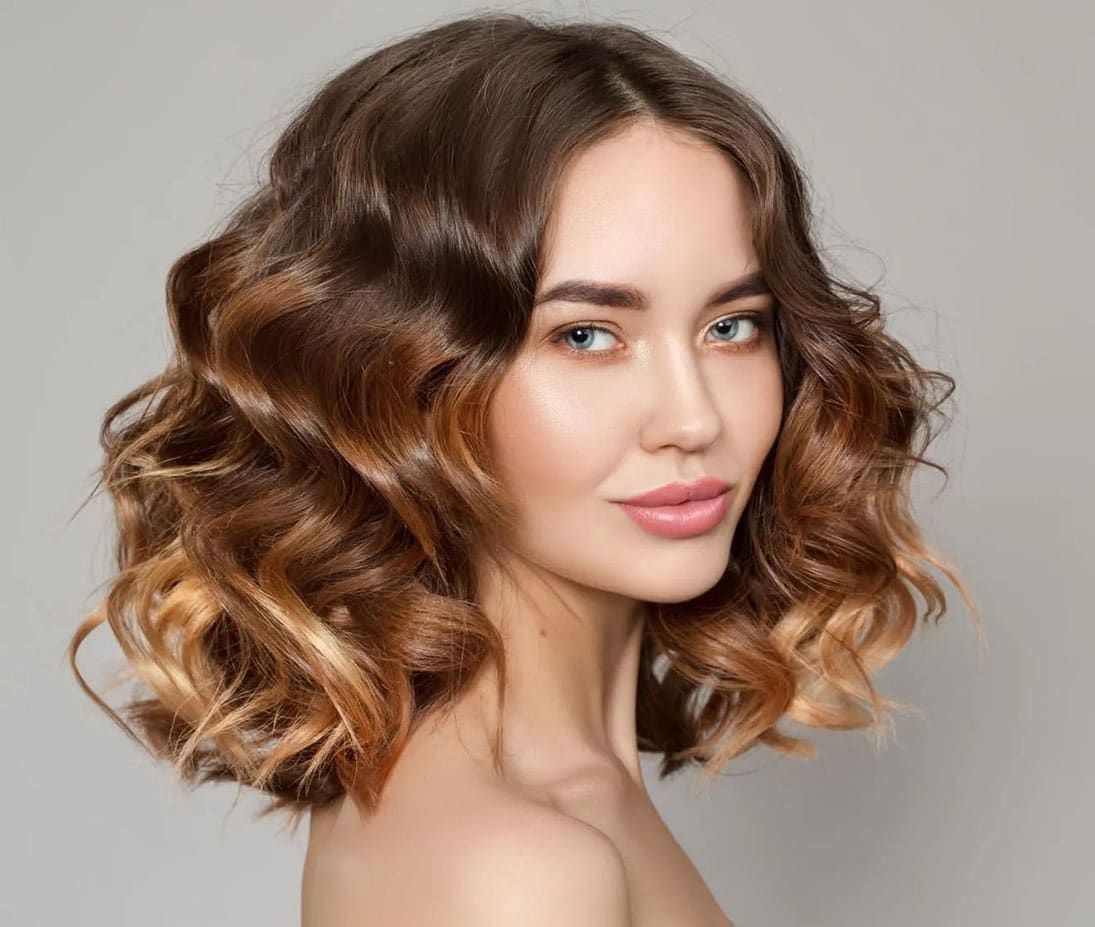 A Woman With Curly Hair is Smiling and Looking at the Camera — Sophisticut Hair Salon in Mysterton, QLD