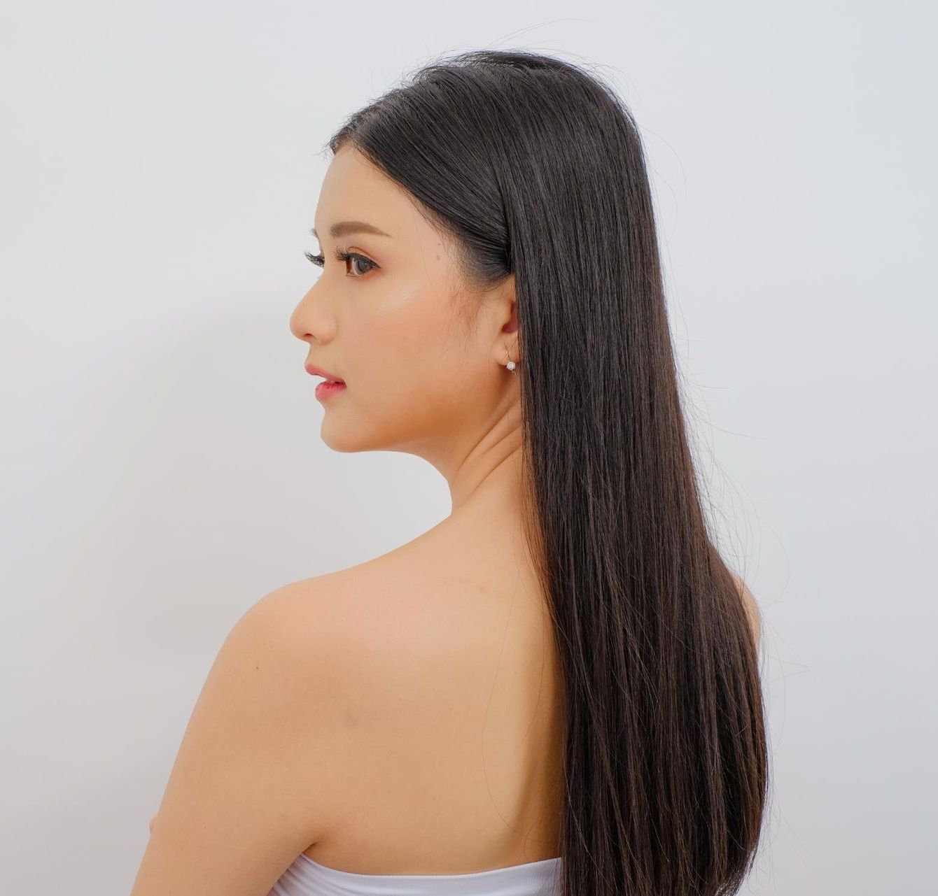 A Woman With Long Hair is Standing in Front of a White Wall — Sophisticut Hair Salon in Mysterton, QLD