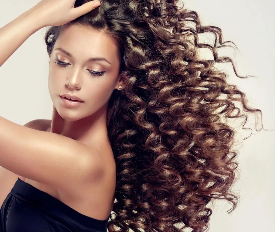 A Woman With Long Curly Hair is Holding Her Hair in Her Hand — Sophisticut Hair Salon in Mysterton, QLD