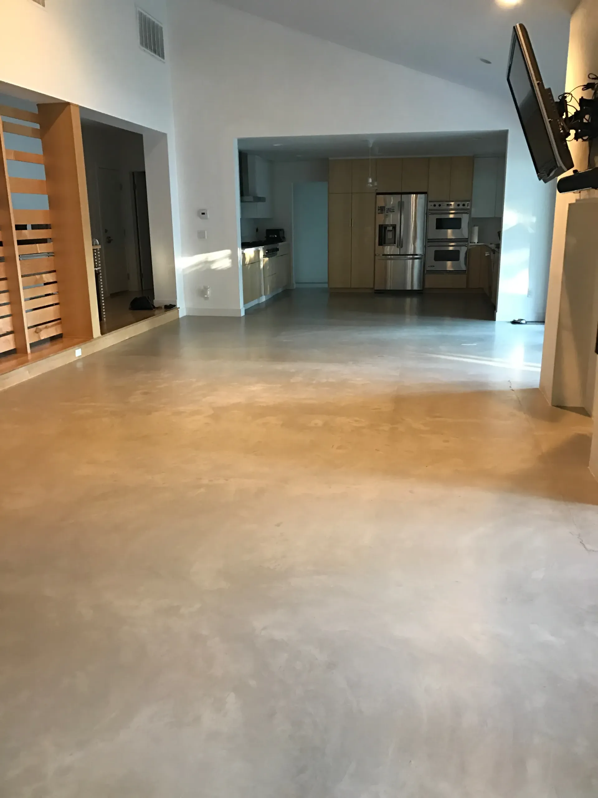 A living room with a concrete floor and a kitchen in the background.