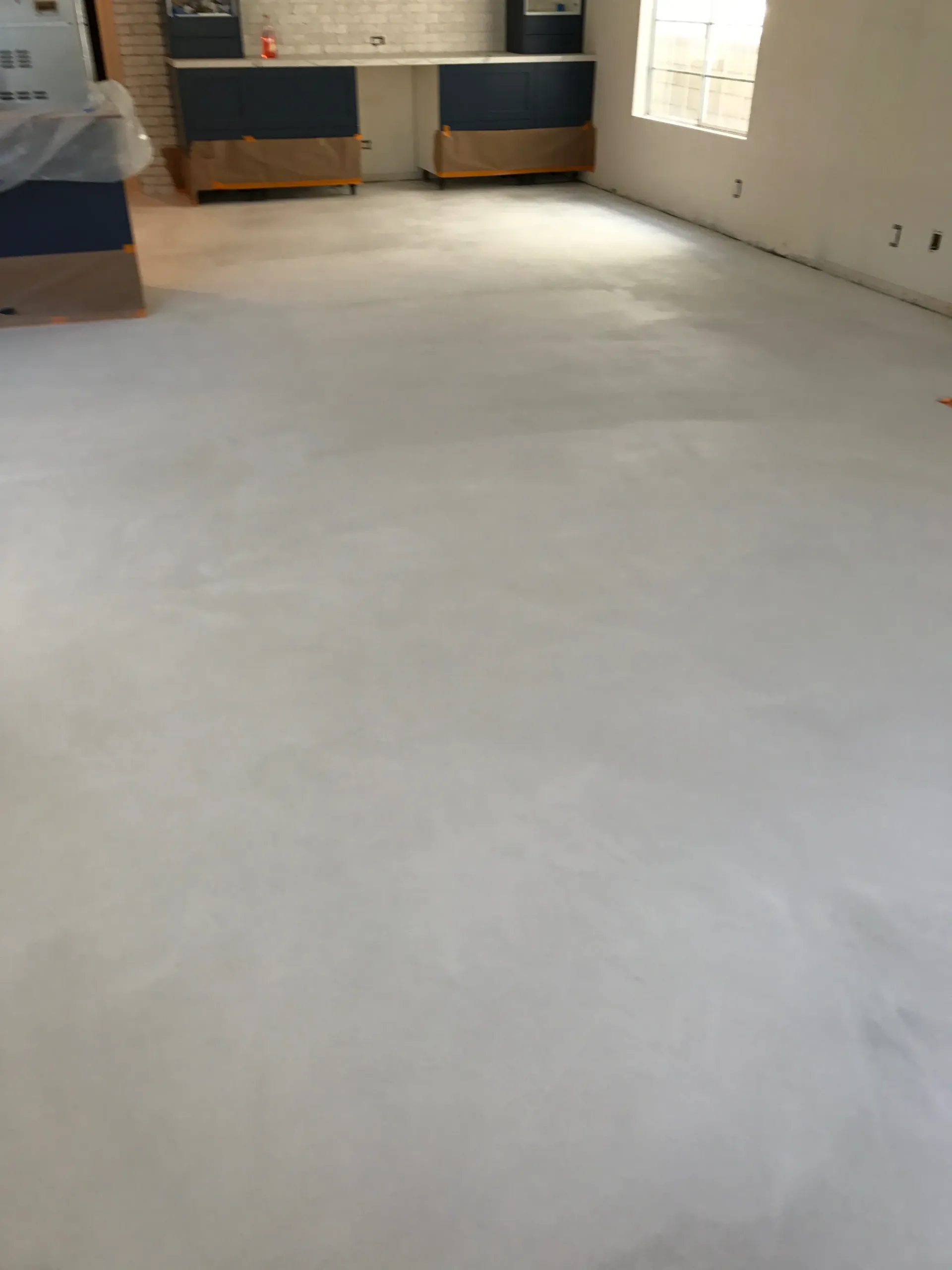 A room with a white floor and a kitchen in the background.