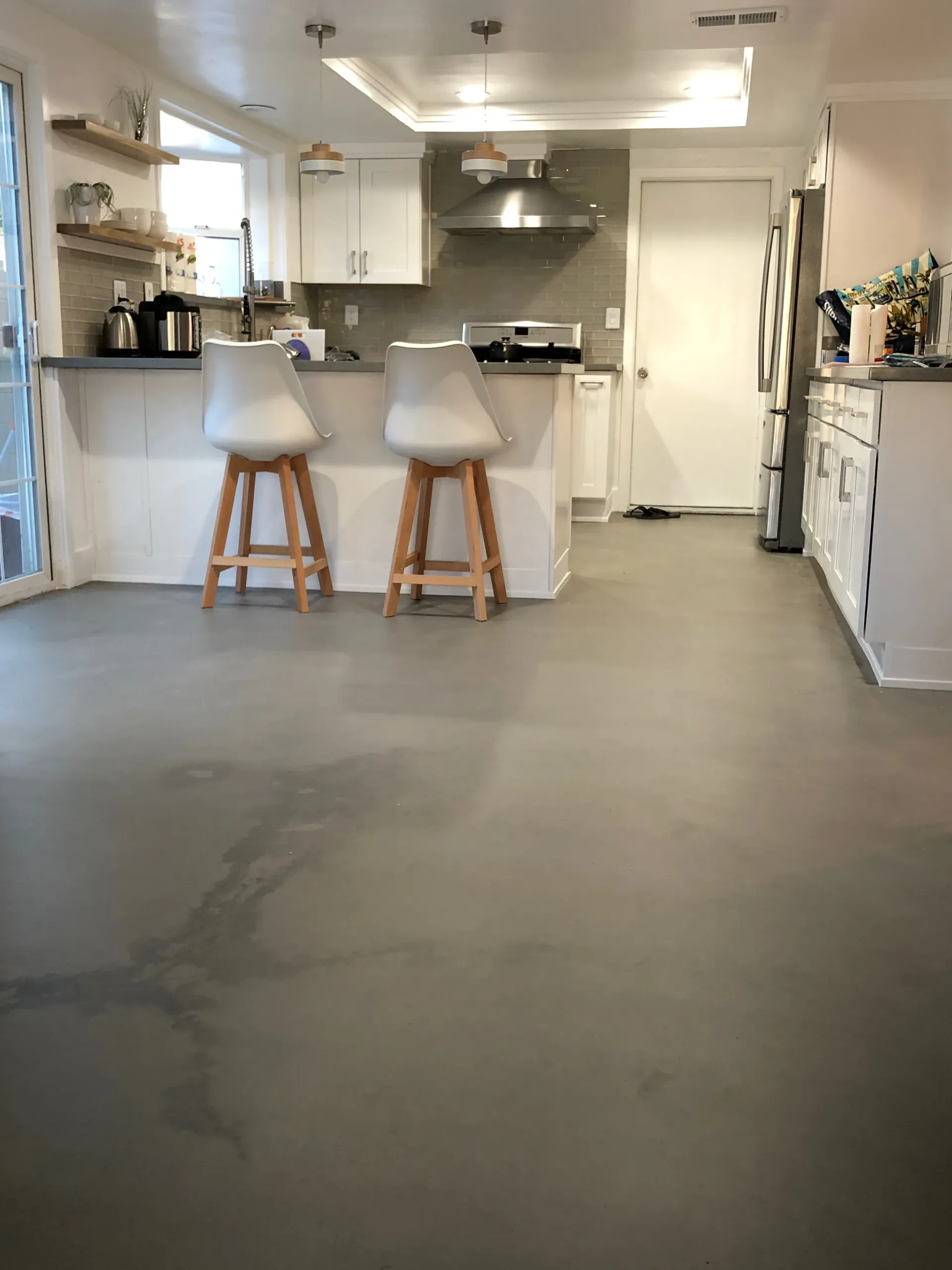 A kitchen with a concrete floor and two stools on the island.