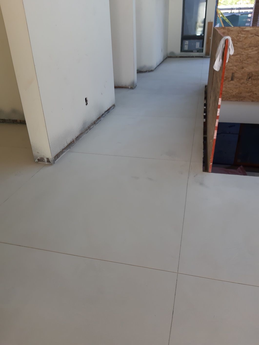A white tile floor in a room with a staircase in the background.