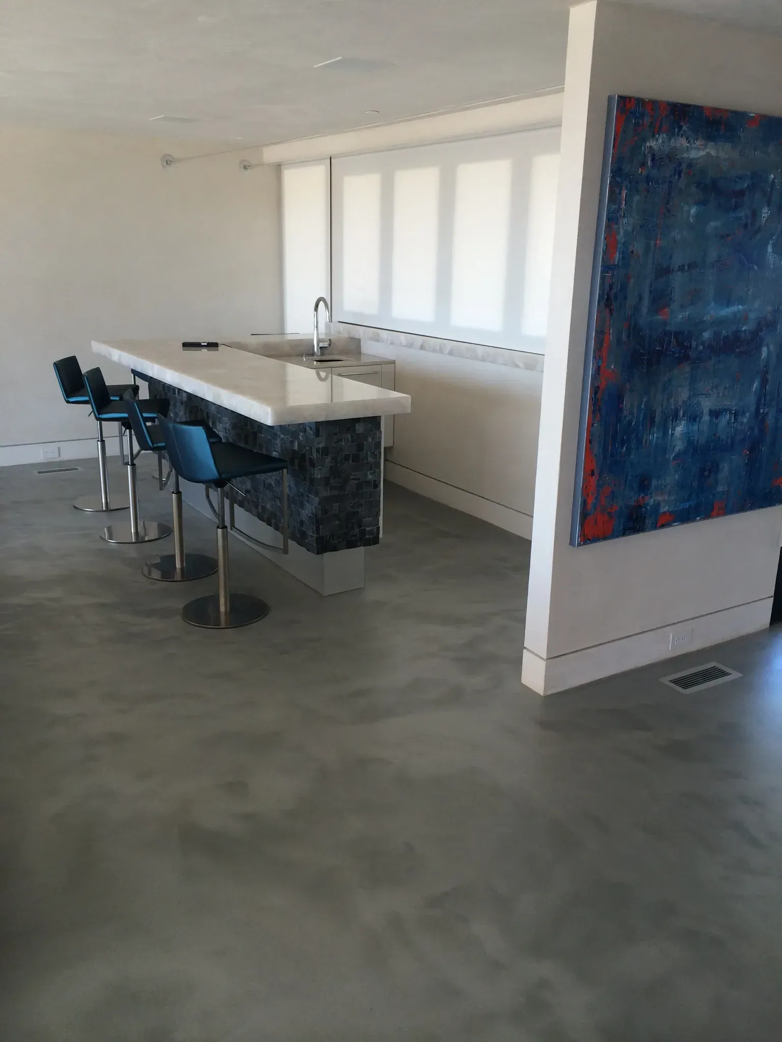 A kitchen with a bar and stools and a large painting on the wall.