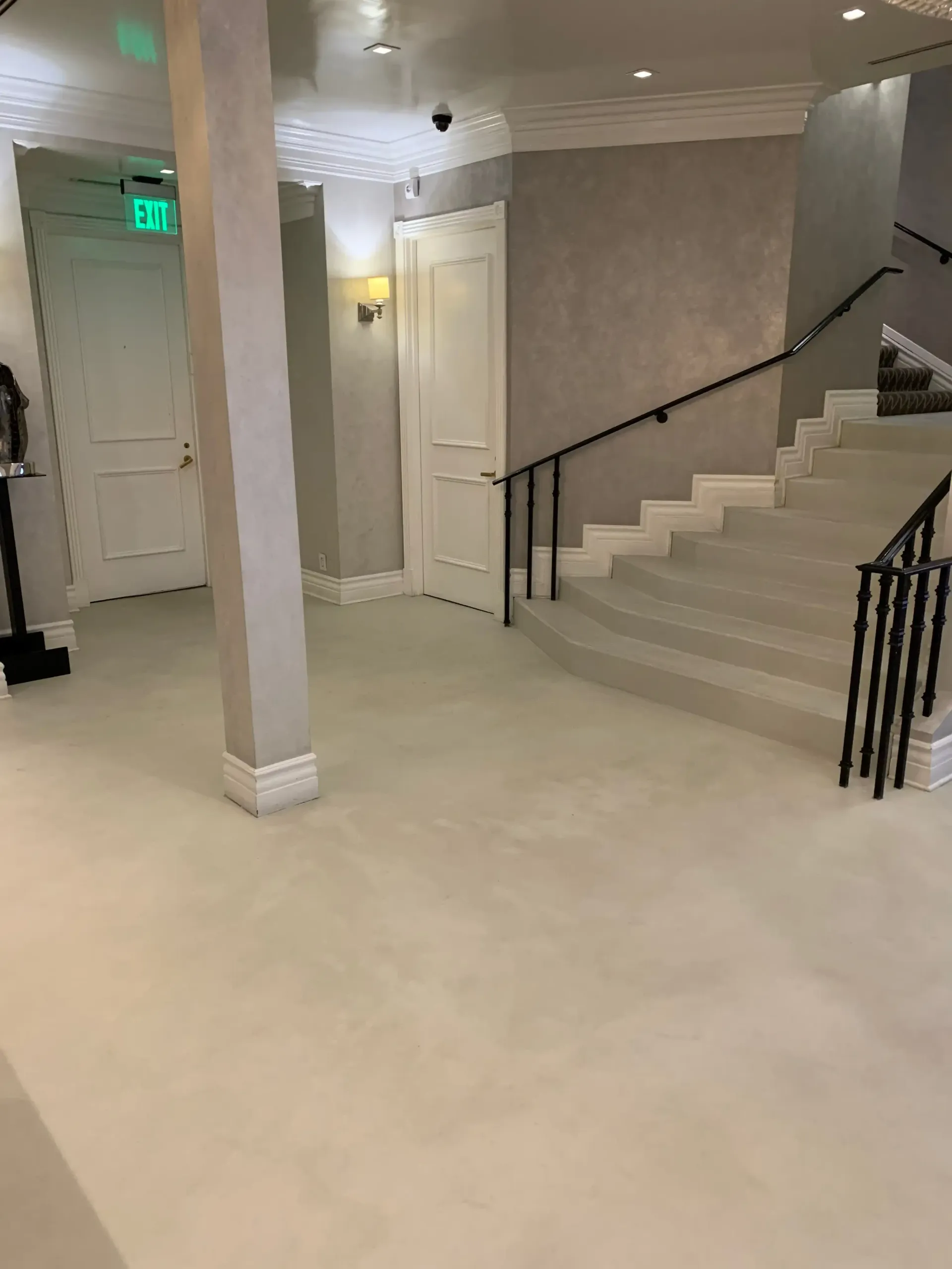 A hallway with stairs and a green exit sign.