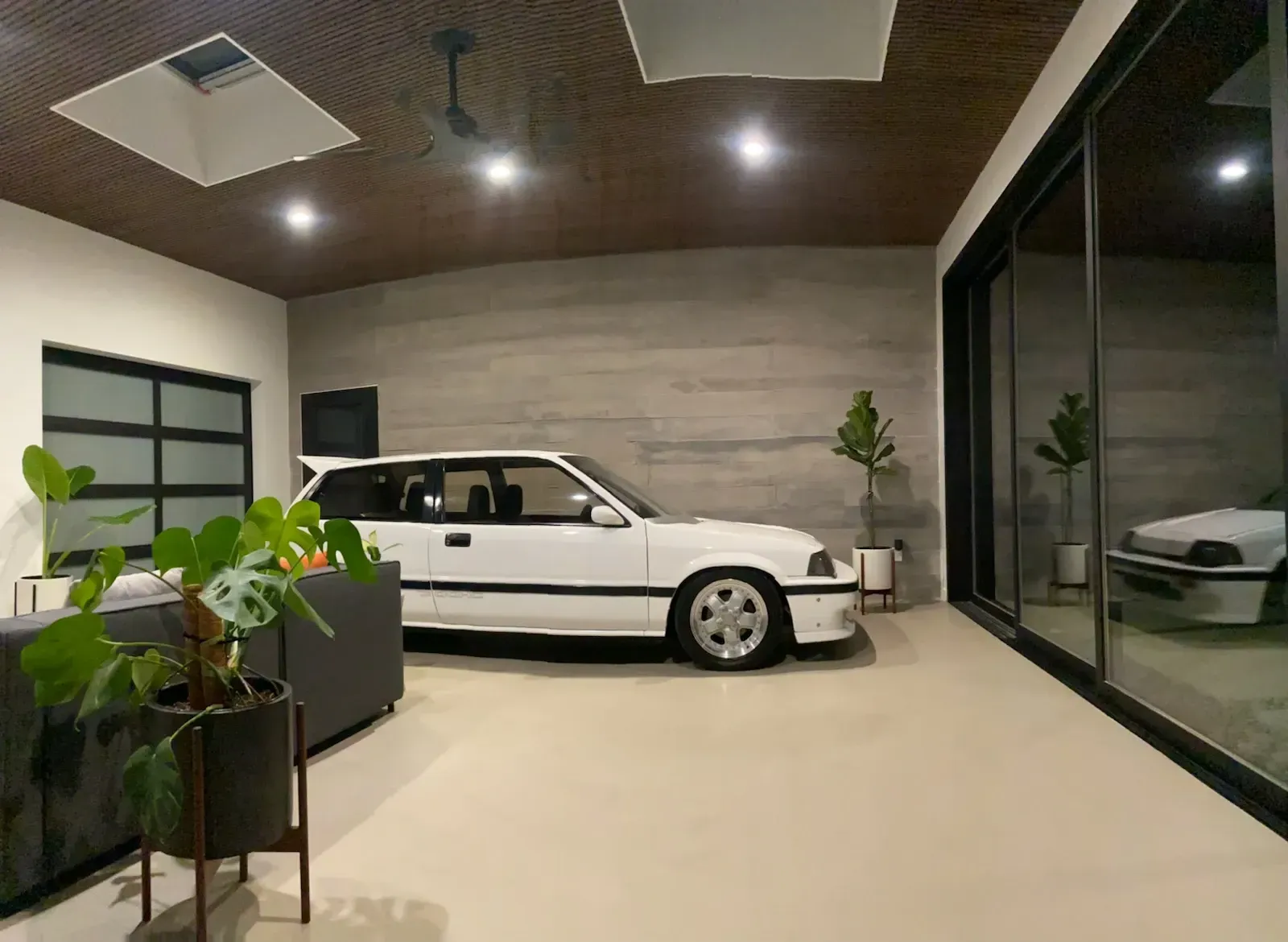 A white car is parked in a garage next to a living room.