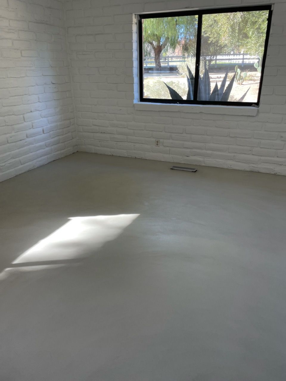 An empty room with a window and a brick wall.