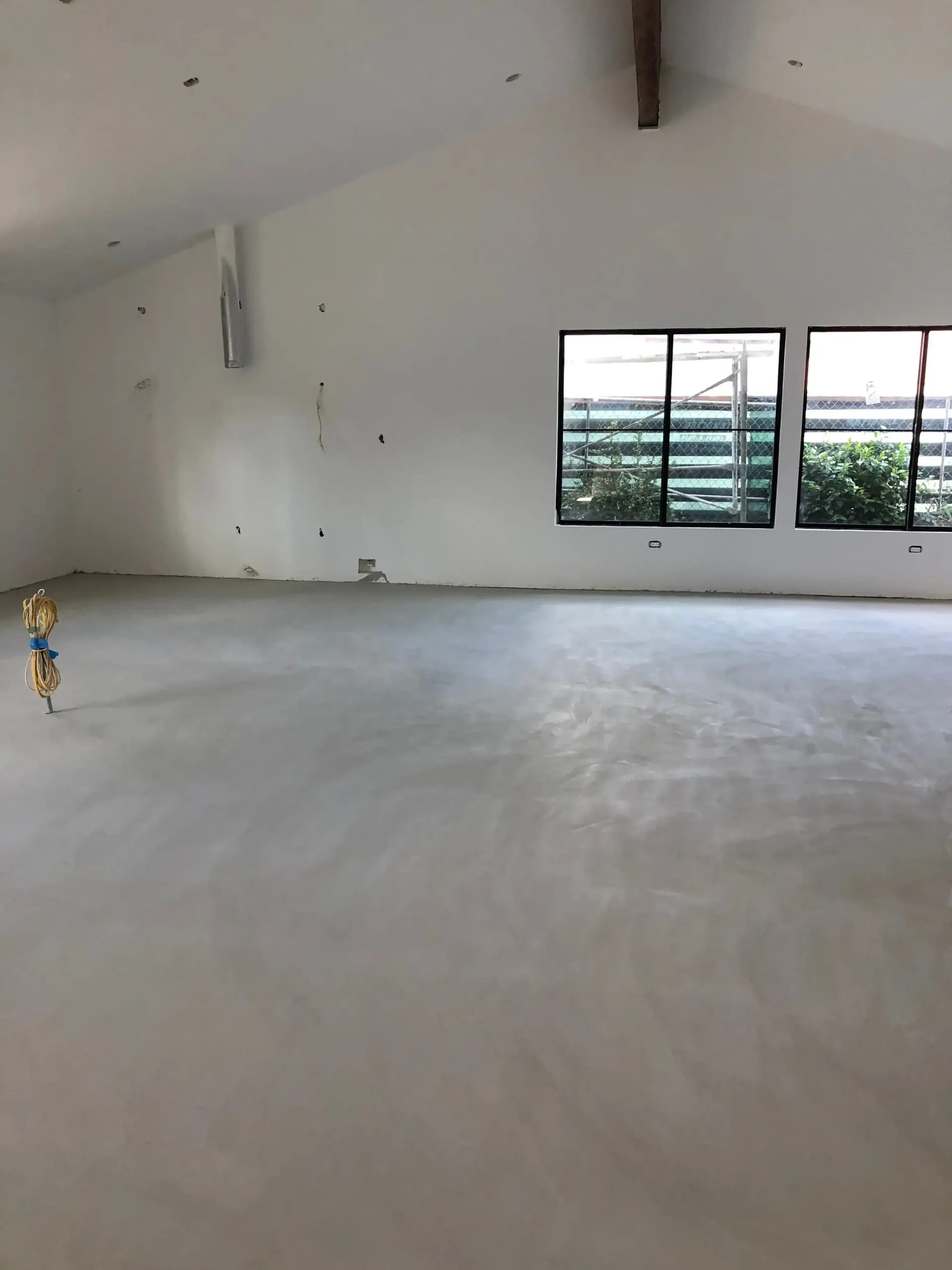 A large empty room with a concrete floor and two windows.