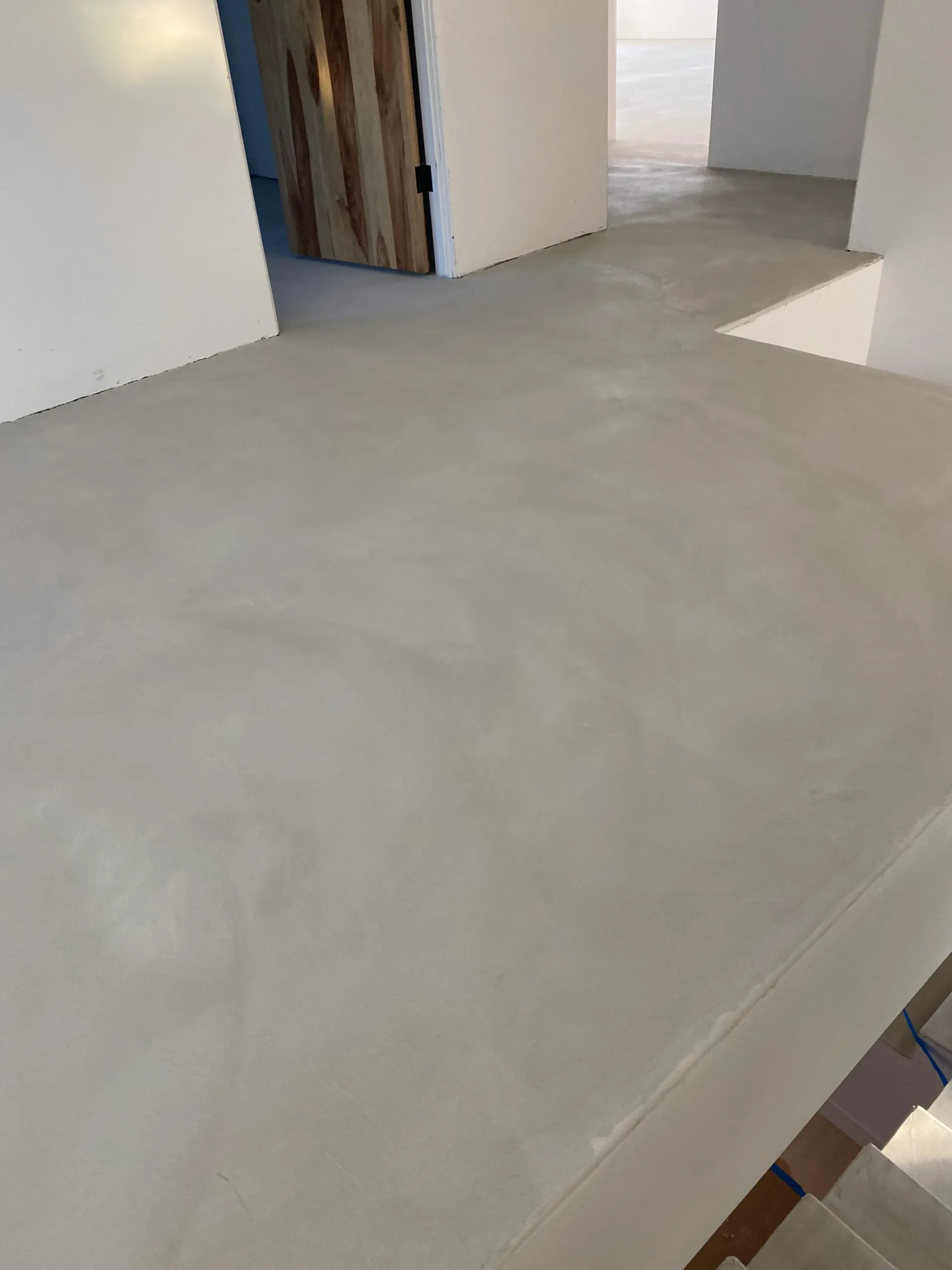 A concrete floor in a room with white walls and stairs.