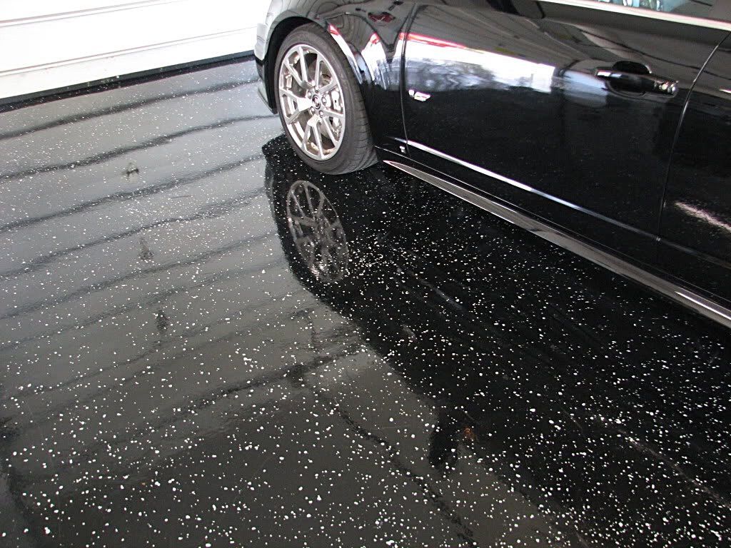 A black car is parked in a garage with a black floor.