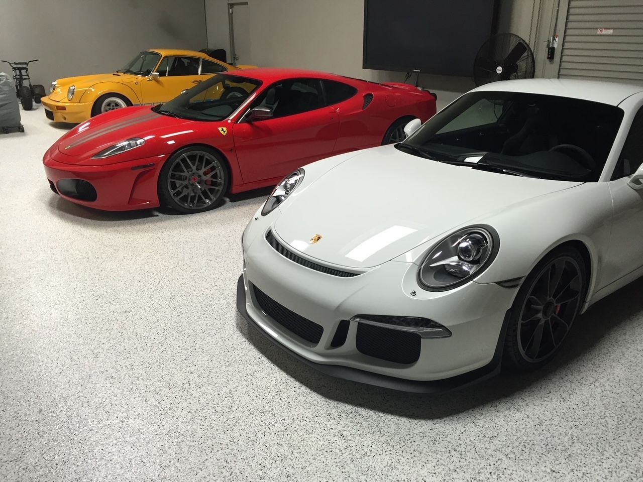 Three sports cars are parked in a garage including a red ferrari and a white porsche