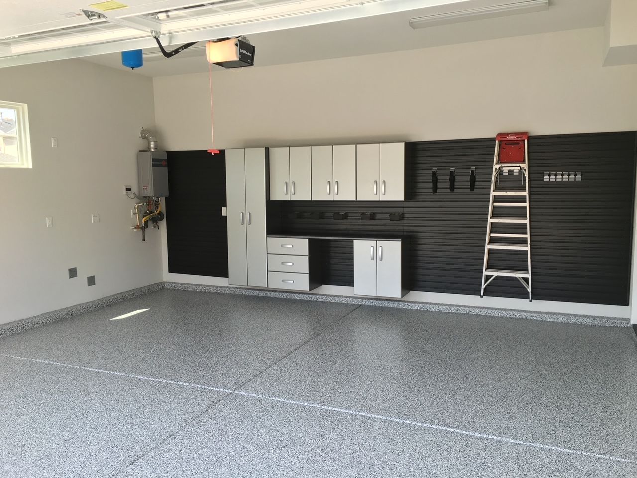 A large empty garage with a ladder and cabinets.