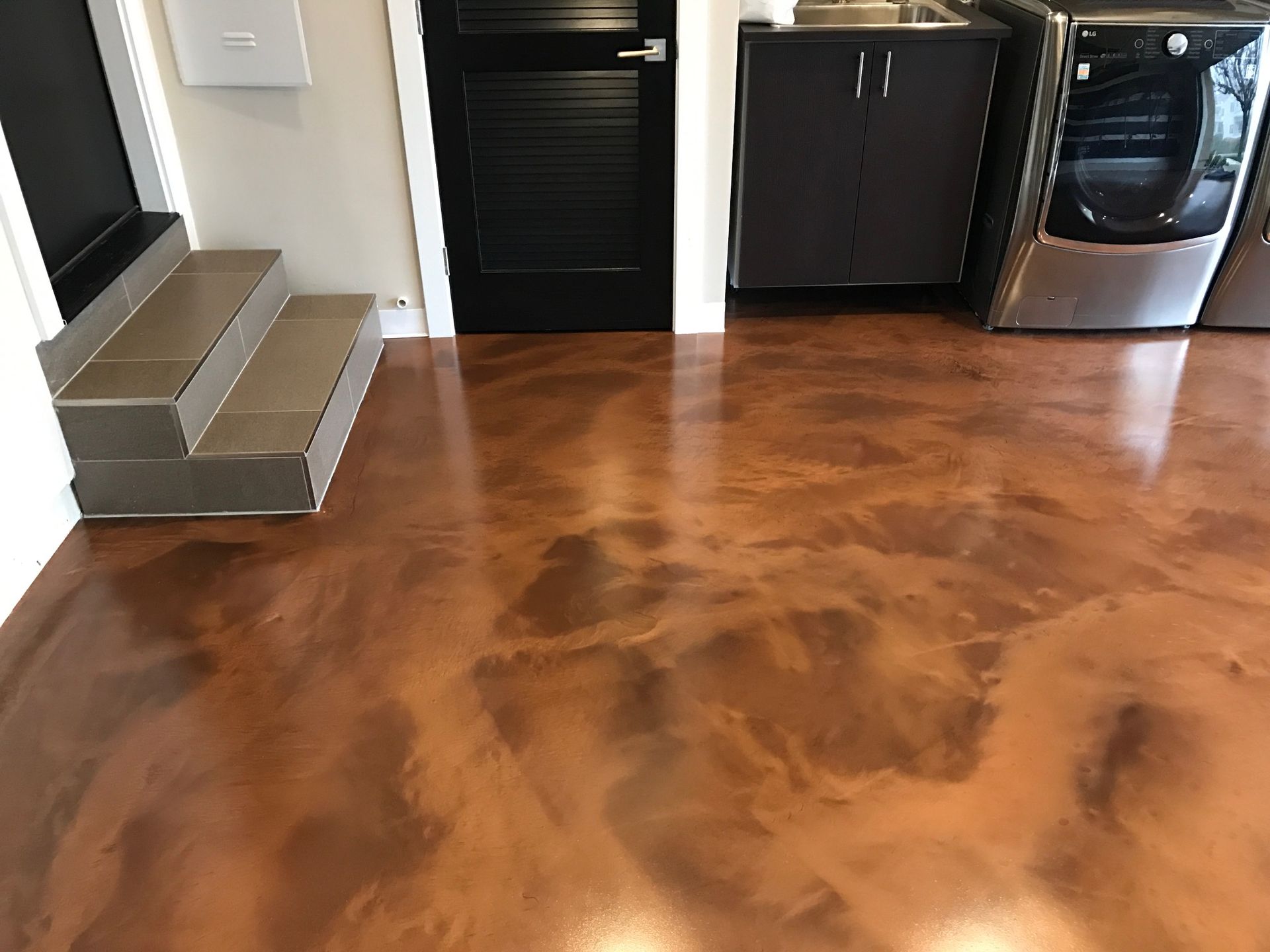 A laundry room with a copper colored floor and stairs leading up to it.
