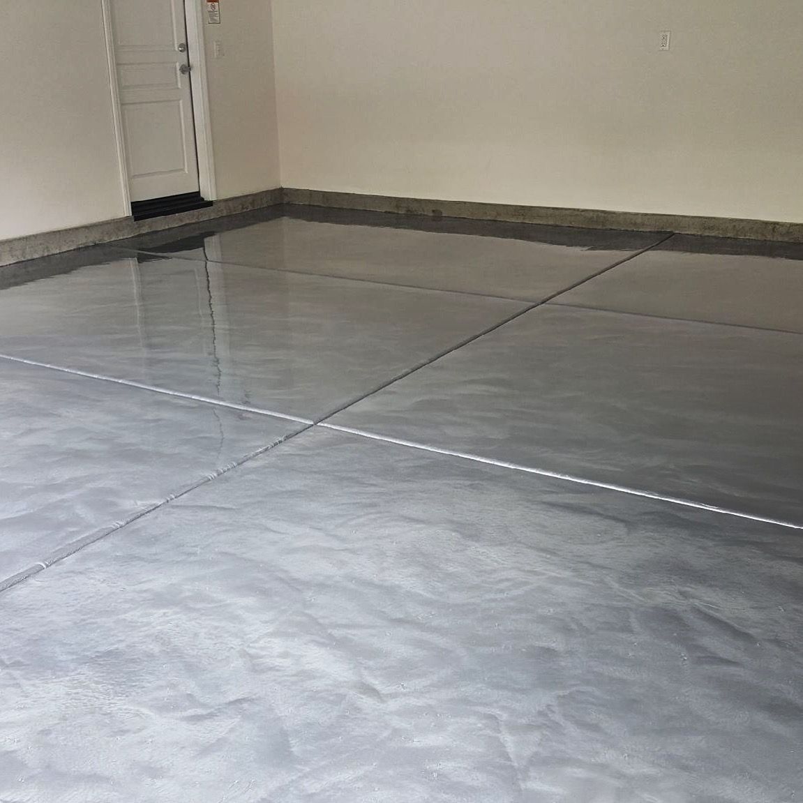 A gray metallic floor in a garage with a door in the background.