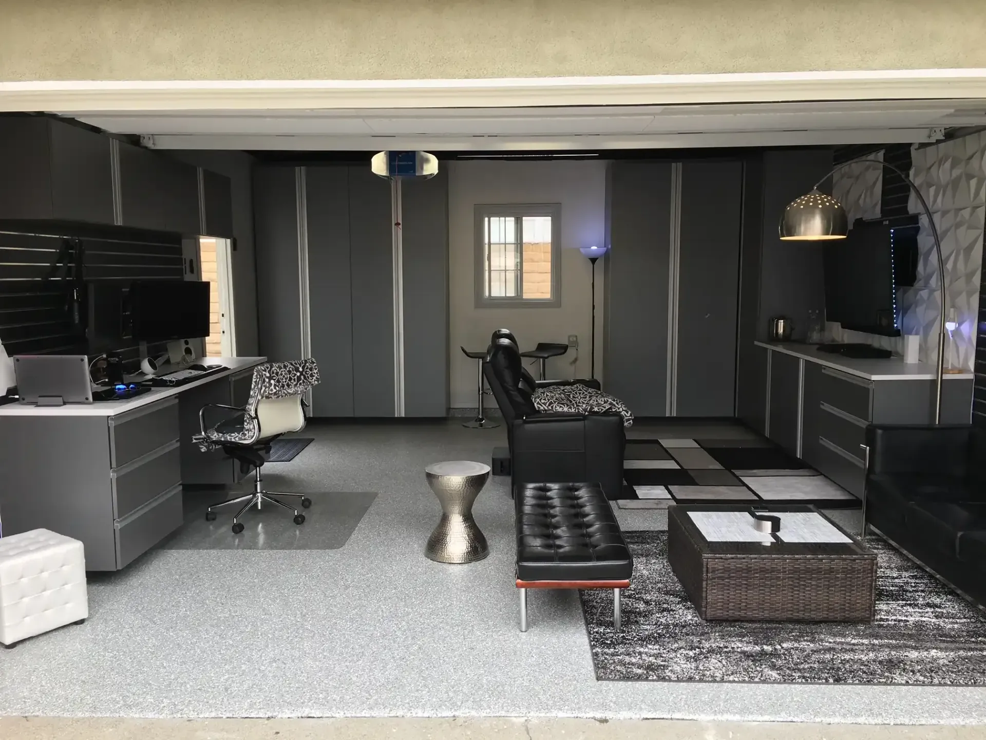A garage turned into a living room with a couch , desk , chair , and coffee table.