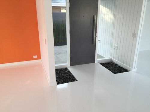 An empty room with a white floor and a black door.