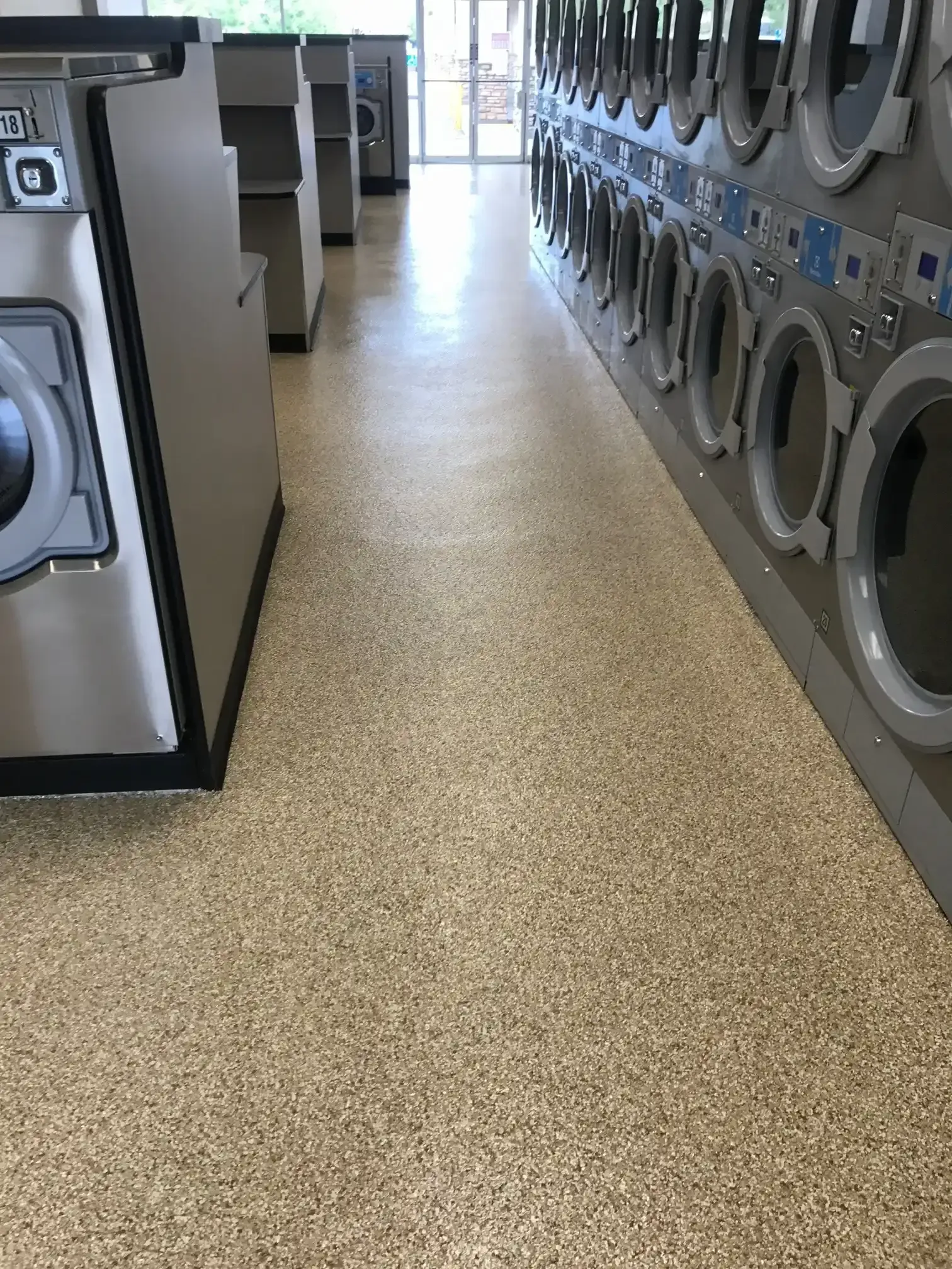 A row of washing machines in a laundromat with a concrete floor.