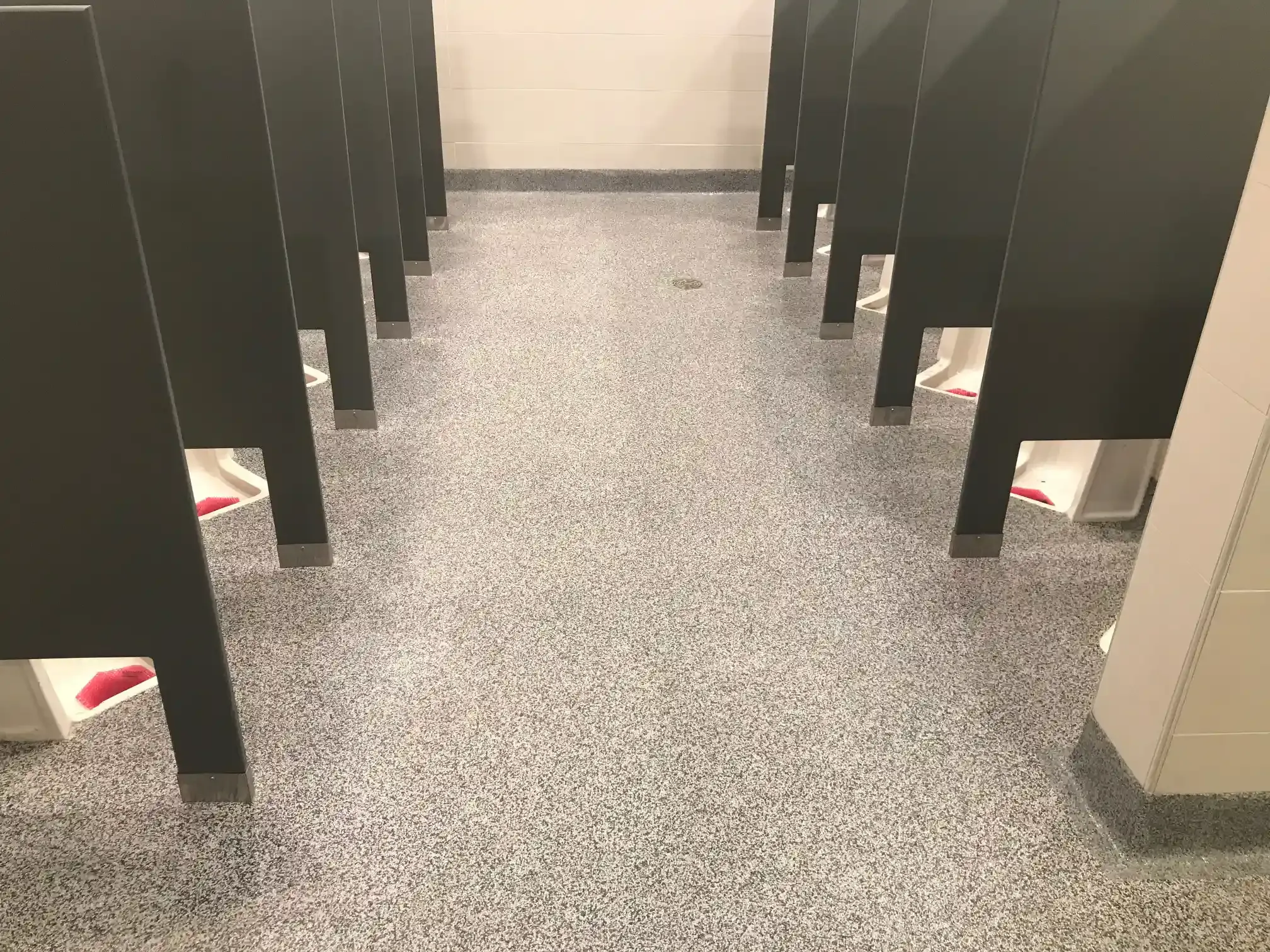 A row of toilet stalls in a public restroom with a gray floor.