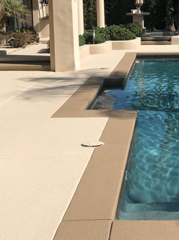 A swimming pool with a concrete deck and a fountain in the background