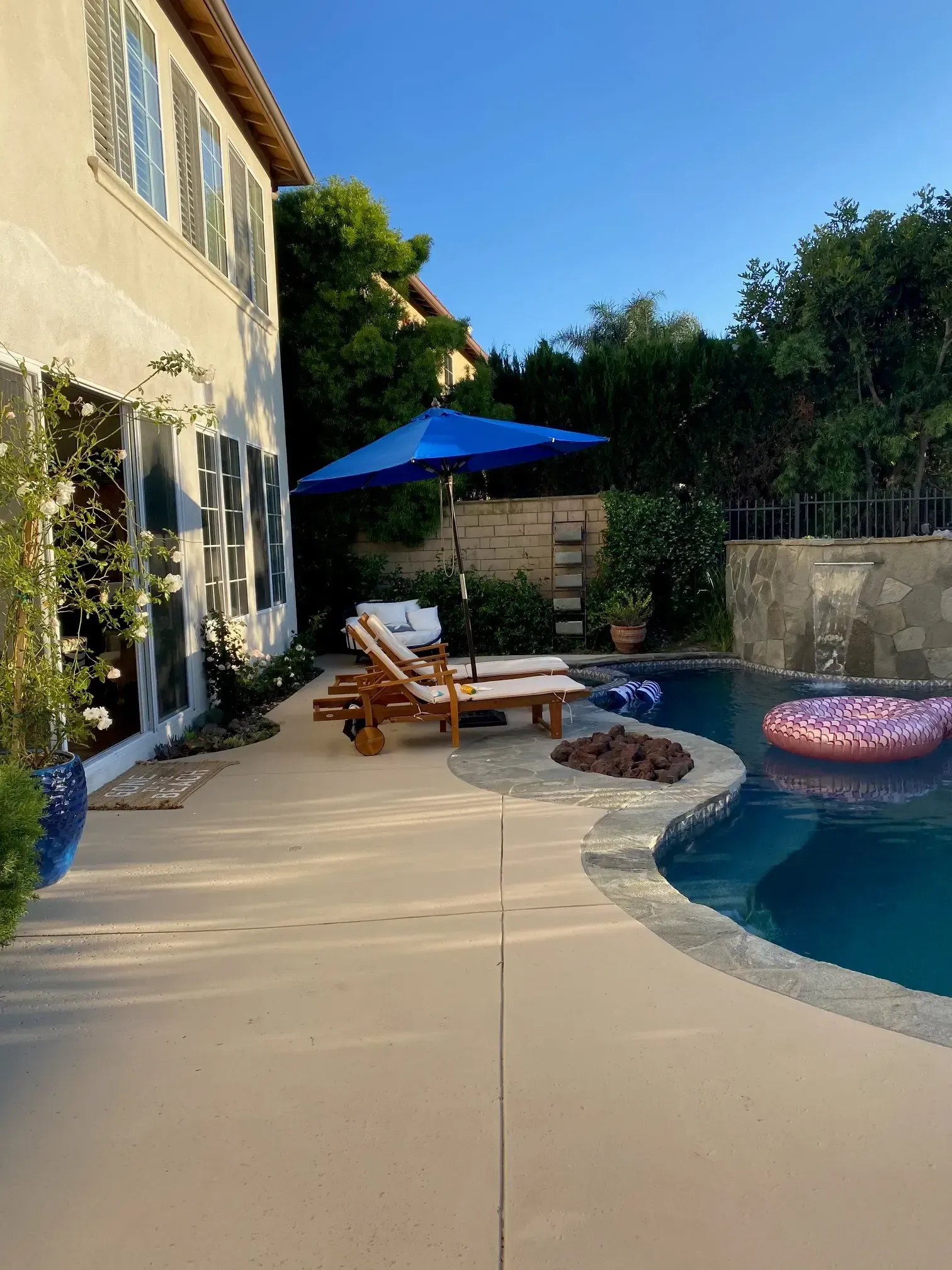 A swimming pool with a blue umbrella and chairs in front of a house.