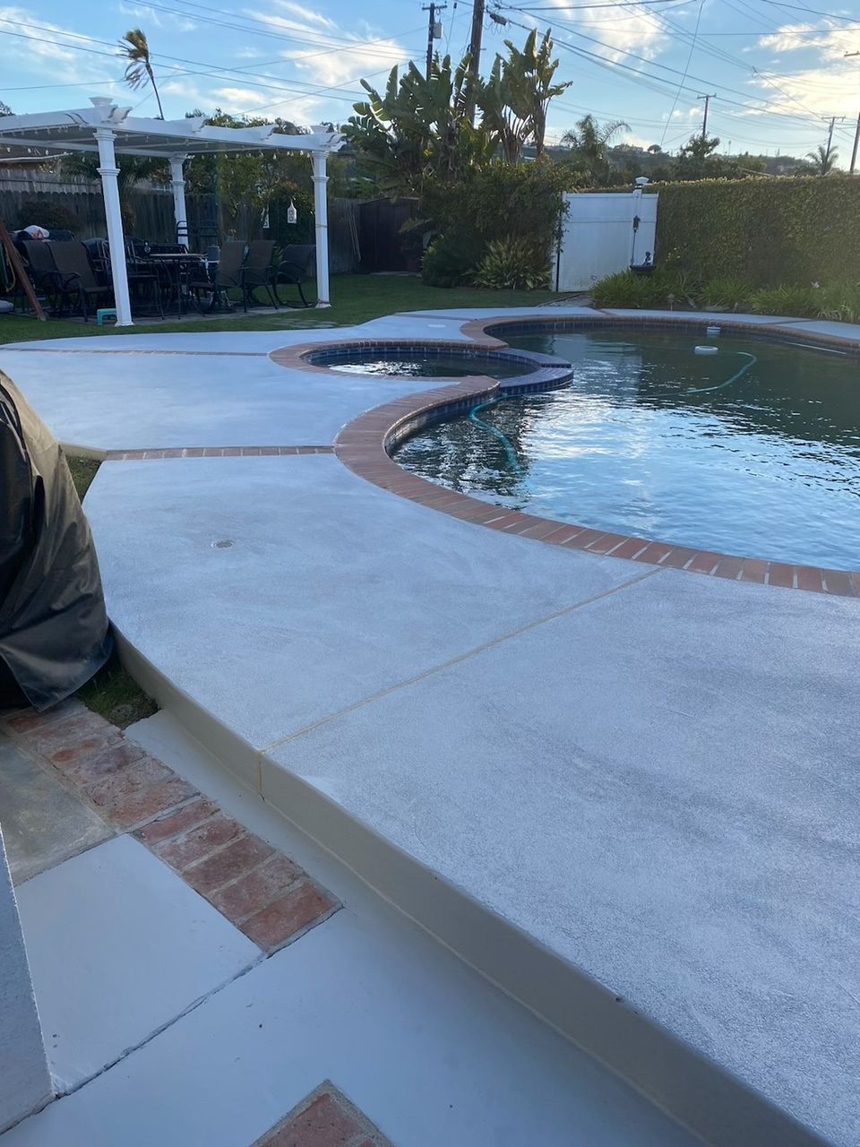 A man is working on a concrete deck next to a swimming pool.