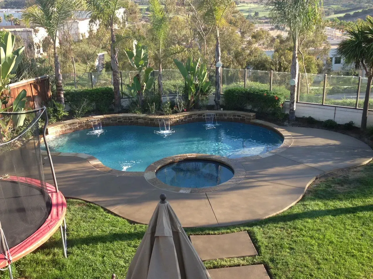A large swimming pool with a trampoline in the backyard
