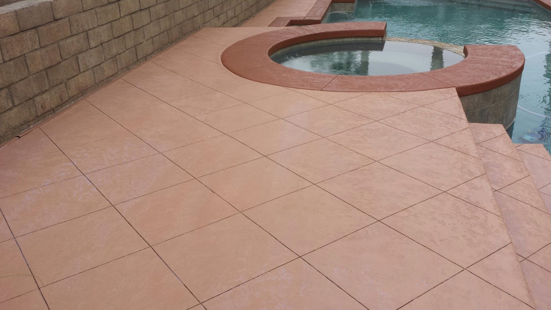 A patio next to a swimming pool with a hot tub in the middle.