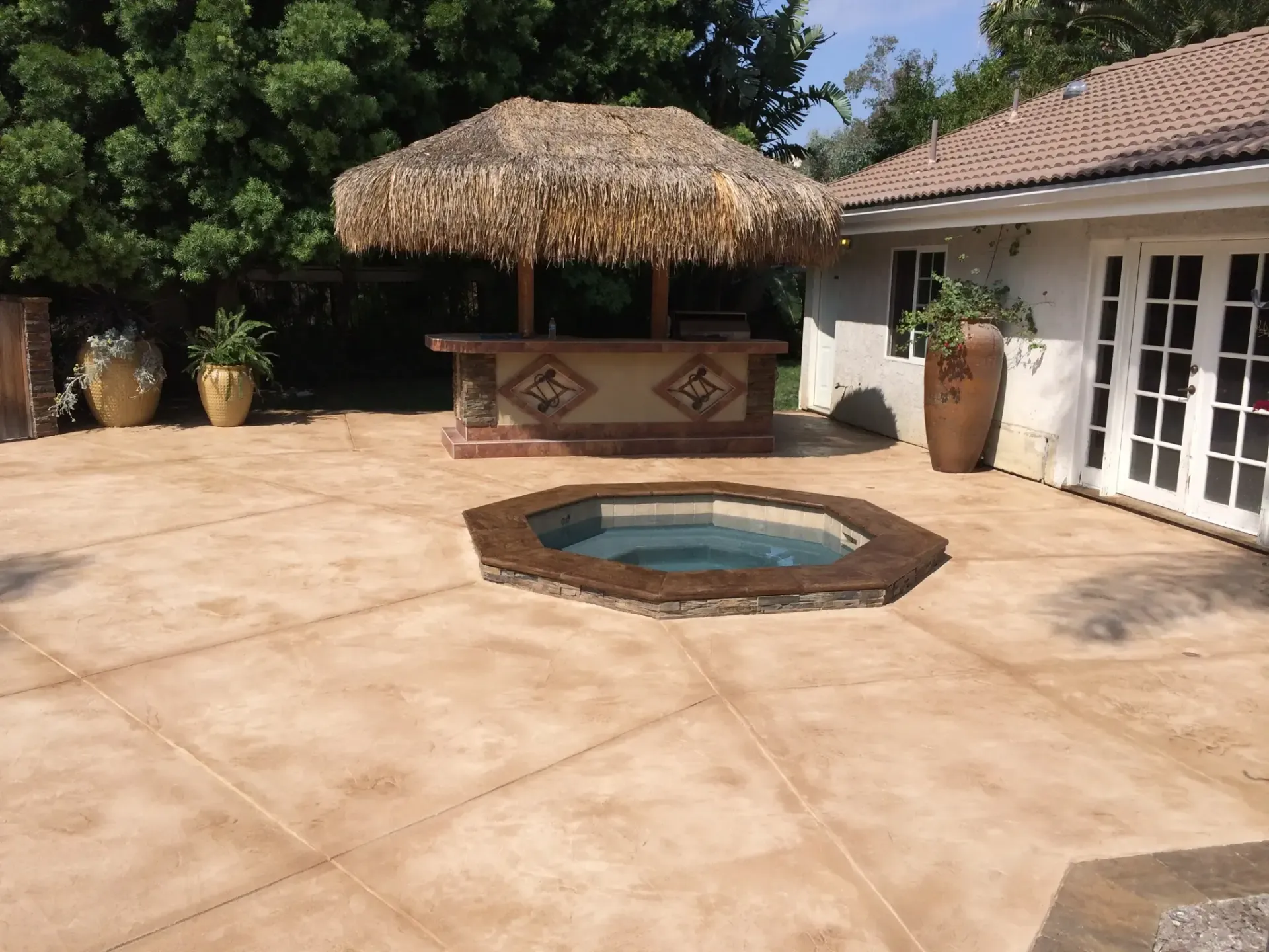 A patio with a hot tub and a thatched hut