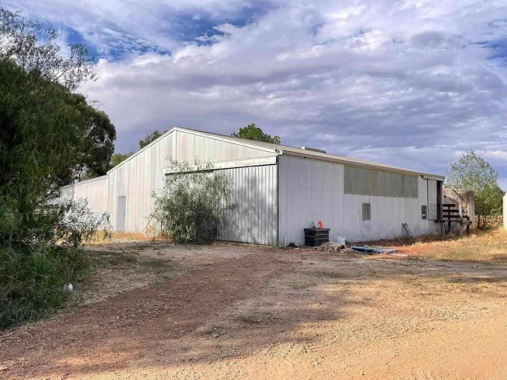 A Large White Building Is Sitting in The Middle of A Dirt Field — Bay Coast Electrical & Control Solutions in Maloneys Beach, NSW